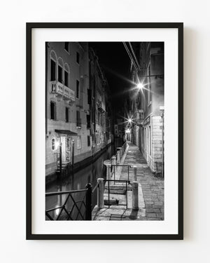 Narrow Venice canal at night illuminated by street lamps in black and white