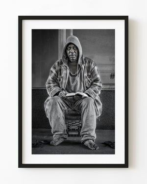 New York street portrait of a seated man holding an open book in black and white