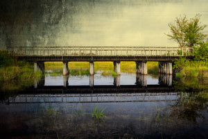 Textured colour photograph of a low bridge and its reflection