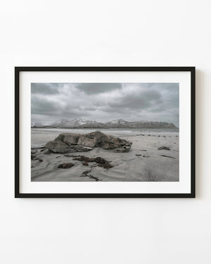 Weathered rocks on a Norwegian beach beneath snowy mountains
