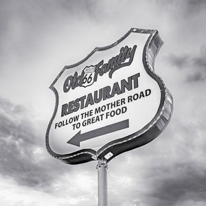 Shield-shaped roadside restaurant sign beneath cloudy skies