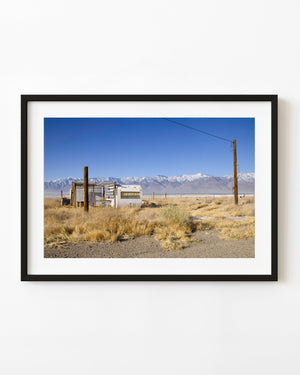 Old trailer beneath snowy mountains and a clear blue sky