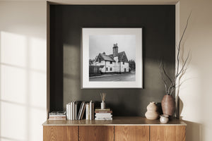Framed black and white photograph of a house on a wall above a wooden cabinet with decorative items.