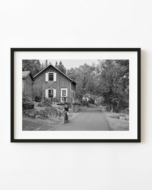Boy riding a bicycle past wooden homes in an Ontario village, black and white