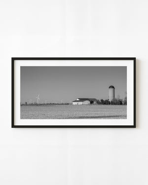 Ontario farm buildings and a tall silo beside distant wind turbines, black and white