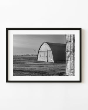 Metal barn and concrete silo with distant Ontario wind turbines, black and white