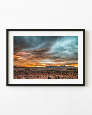 Orange sunset clouds above a broad Southwest desert and distant mountains