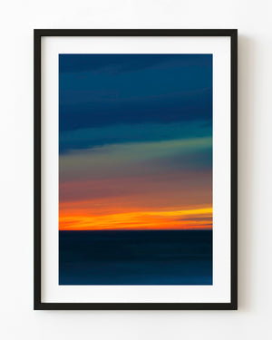 Orange sunset light along a dark ocean horizon beneath deep blue clouds