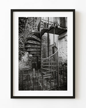 Ornate iron spiral staircase beside ivy-covered stone walls, black and white
