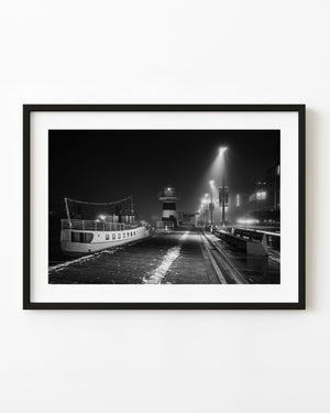 Moored boat and striped beacon beside Oslo’s misty Aker Brygge waterfront at night