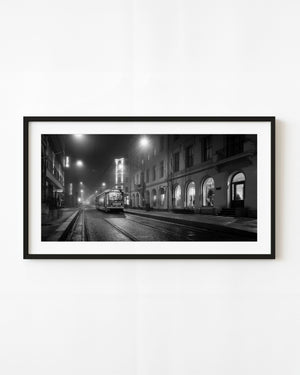 Oslo tram on a wet street beneath glowing lamps at night, black and white