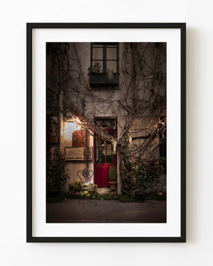 Red Paris bistro door and an empty iron chair beneath climbing vines at night
