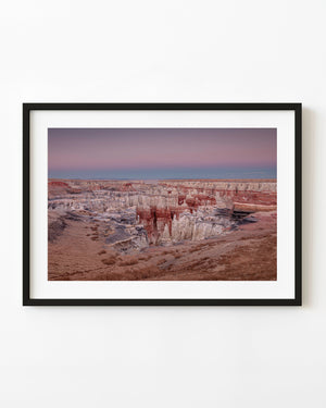 Pastel canyon layers and red-white rock spires beneath a pink sky