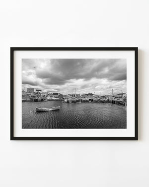 Peggy’s Cove harbour buildings and a small boat beneath cloudy skies, black and white
