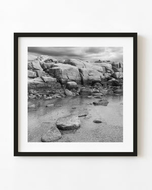 Large granite boulders beside shallow water at Peggy’s Cove, black and white