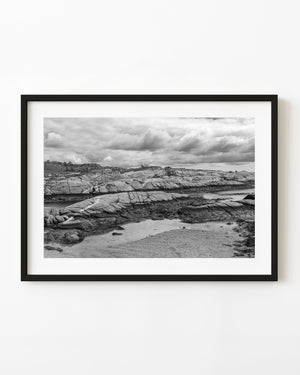 Peggy’s Cove rock shelves and shallow tidal water beneath clouds, black and white