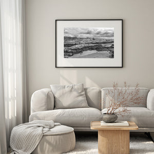 Black and white coastal scene with shallow pools and layered granite