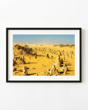 Limestone pinnacles scattered across golden desert sand beneath a blue sky