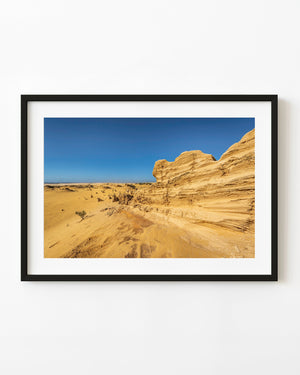 Layered golden rock formation beside dunes in the Pinnacles Desert