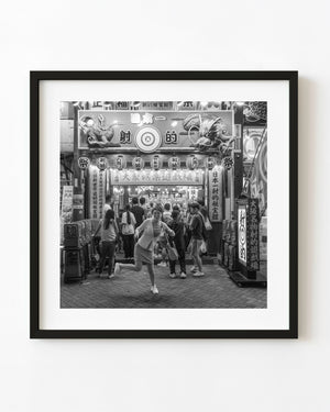 Woman posing playfully outside a brightly lit Osaka shooting gallery at night