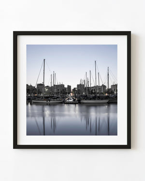 Sailboats moored at Port Vell in Barcelona beneath a pale blue dawn sky