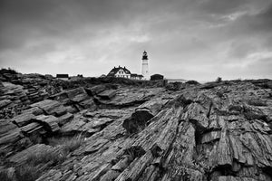 White lighthouse and keeper’s house beyond deeply layered shoreline rocks
