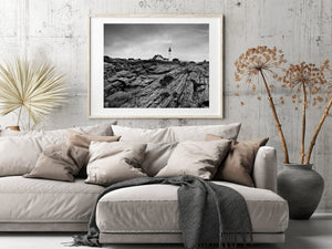 Black and white coastal landscape with a lighthouse above weathered rocks