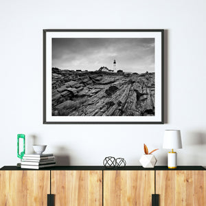 Maine lighthouse standing above sloping rock shelves under an overcast sky