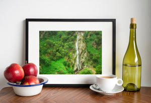 Elevated view of a slender waterfall falling through a rugged wooded hillside
