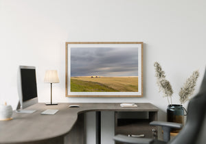 Prairie harvest scene with distant combines under sweeping grey clouds