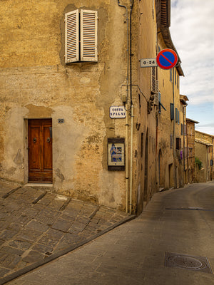 Narrow downhill street in Tuscany village with historic buildings and shutters