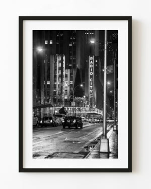 Radio City Music Hall illuminated above New York traffic at night in black and white