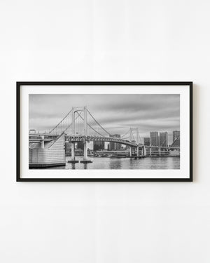 Rainbow Bridge spanning Tokyo Bay beneath a cloudy sky in black and white