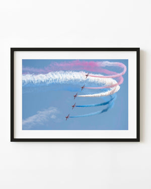 Red Arrows jets turning with red, white and blue smoke trails against a blue sky