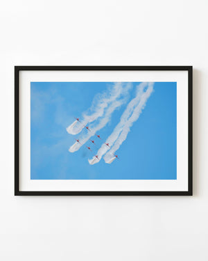 Red Arrows aircraft in formation beneath curling white smoke against a blue sky