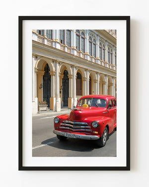 Red classic Havana taxi passing beneath sunlit colonial arches