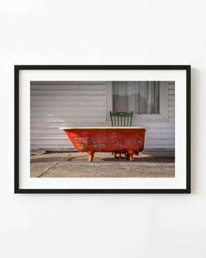 Weathered red clawfoot bathtub outside a Route 66 motel with a green chair behind it