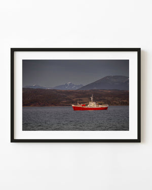 Red-hulled ship sailing near Ushuaia beneath dark mountains and an overcast sky