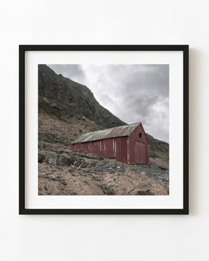 Weathered red Lofoten boathouse beneath a steep rocky mountainside