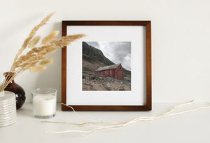 Red coastal building surrounded by boulders and rough grass