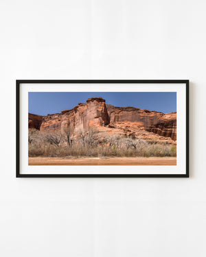 Red sandstone cliffs streaked with dark desert varnish beneath a clear blue sky
