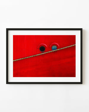 Two round portholes in a bright red ship hull crossed by a diagonal rope