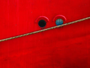 Weathered red hull with twin circular windows and a thick mooring rope
