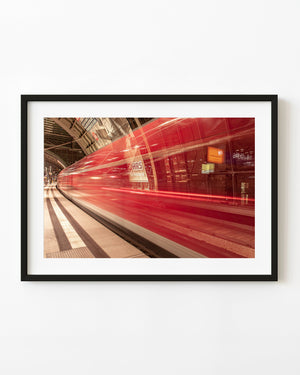 Red train blurred in motion beside a platform at Dresden station