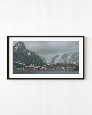 Reine village lights beneath snowy Norwegian mountains across a quiet evening bay