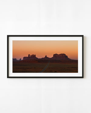 Road leading toward Monument Valley buttes beneath a warm orange sunrise