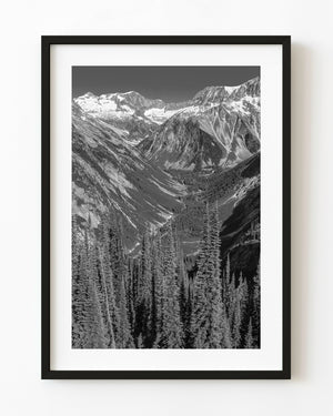 Forested Rocky Mountain valley beneath snow-covered peaks in black and white