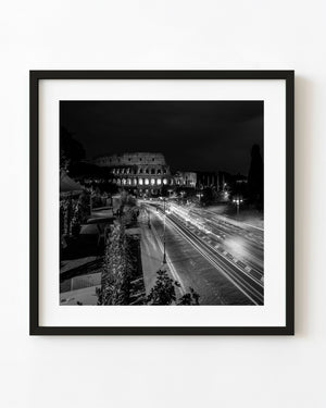 Roman Colosseum illuminated at night above sweeping traffic trails in black and white