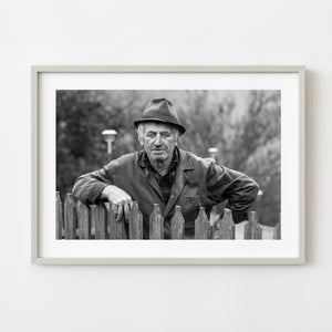 black and white portrait of rural Romanian farmer leaning on wooden fence