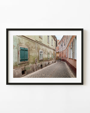 Figure walking down a Romanian cobbled lane between weathered colourful buildings